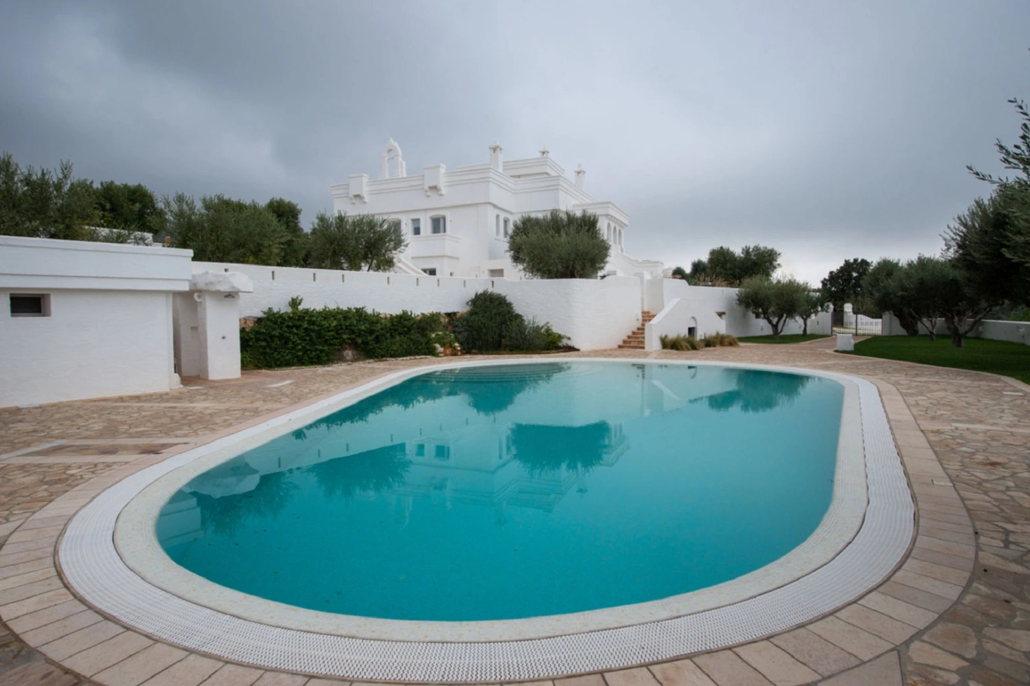 Owalny basen z błękitną wodą otoczony chodnikiem od Marazzi